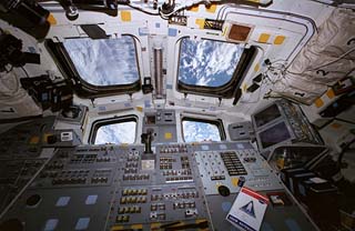 View of the aft flight deck controls on the STS-79 shuttle Atlantis with a cloudy Earth visible in all the overhead windows. 